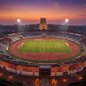 A majestic aerial view of Thrissur Municipal Corporation Stadium illuminated at dusk, with the iconic Vadakkumnathan Temple visible in the background. The stadium's modern floodlights create dramatic light beams against the deep purple-orange sky. Traditional Kerala-style architectural elements blend seamlessly with contemporary design features. The stadium's running track appears in vibrant terracotta red, while the lush green football field creates a striking contrast. Multiple sports activities are depicted simultaneously - athletes training on the track, footballers practicing, and spectators in the modernized grandstand. Intricate Madhubani-style patterns decorate the stadium's exterior walls in gold and peacock blue. Small glowing diyas and traditional Kerala oil lamps line the stadium's entrance pathway. The scene includes floating mandala patterns in the sky, rendered in soft golden light. The overall composition combines both drone-view and artistic perspective, with a photorealistic style enhanced by magical realism. The lighting creates a dramatic interplay of shadows and highlights, while maintaining the warm, ethereal atmosphere characteristic of Kerala's cultural heritage.