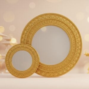 A captivating image of an intricately crafted Aranmula Kannadi, a traditional Indian metal mirror, placed beside a sleek, modern regular mirror. The Aranmula Kannadi is adorned with ornate patterns and motifs in gold, showcasing its cultural significance and heritage. The mirrors are set against a serene background featuring a soft glow of pastel colors—pale pink and warm gold—with subtle hints of traditional Indian architectural elements. The scene exudes a sense of elegance and harmony, highlighting the contrast between tradition and modernity. The lighting emphasizes the reflective surfaces of both mirrors, creating an ethereal and inviting atmosphere. The art style is a blend of traditional Indian art forms with contemporary digital aesthetics, rich in detail and vibrant in color, designed to engage the viewer's curiosity about the cultural significance and uniqueness of the Aranmula Kannadi.
