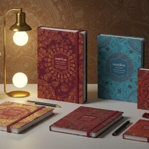 A modern, aesthetically captivating scene featuring an array of Matrikas notebooks and stationery items artfully arranged on a sleek, minimalist desk. The notebooks have intricate covers with digital patterns inspired by traditional Indian art forms like Madhubani and Pattachitra, incorporating motifs such as lotus flowers and mandalas. The color palette is rich and vibrant, with deep maroon, peacock blue, and saffron hues. Soft, ethereal lighting casts a warm glow over the items, creating a serene and inviting atmosphere. In the background, a subtle digital mural blends traditional Indian patterns with modern geometric shapes, emphasizing a sense of innovation and cultural heritage. The overall composition is balanced, highlighting both the elegance and functionality of the stationery products, encouraging readers to explore the guide further.