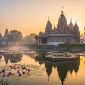 A serene and ethereal depiction of Sitapur's sacred temples, bathed in the soft glow of a golden sunrise. The scene captures a temple complex adorned with intricate carvings and colorful frescoes, reflecting traditional Indian architecture. In the foreground, a calm water surface mirrors the temple spires, surrounded by lush greenery and lotus flowers. A gentle mist adds a surreal atmosphere, while soft pastel hues of blue, pink, and gold envelop the scene. The image conveys a sense of tranquility and spiritual allure, inviting viewers to explore the divine beauty and historical richness of Sitapur's temples.