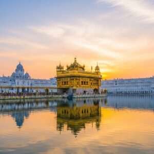 A captivating scene of the Golden Temple in Amritsar during a serene dawn, with the temple's golden facade reflecting beautifully on the calm waters of the surrounding sacred pool. The sky is a blend of soft pastel colors - pale pink, warm gold, and light blue - casting a tranquil glow over the scene